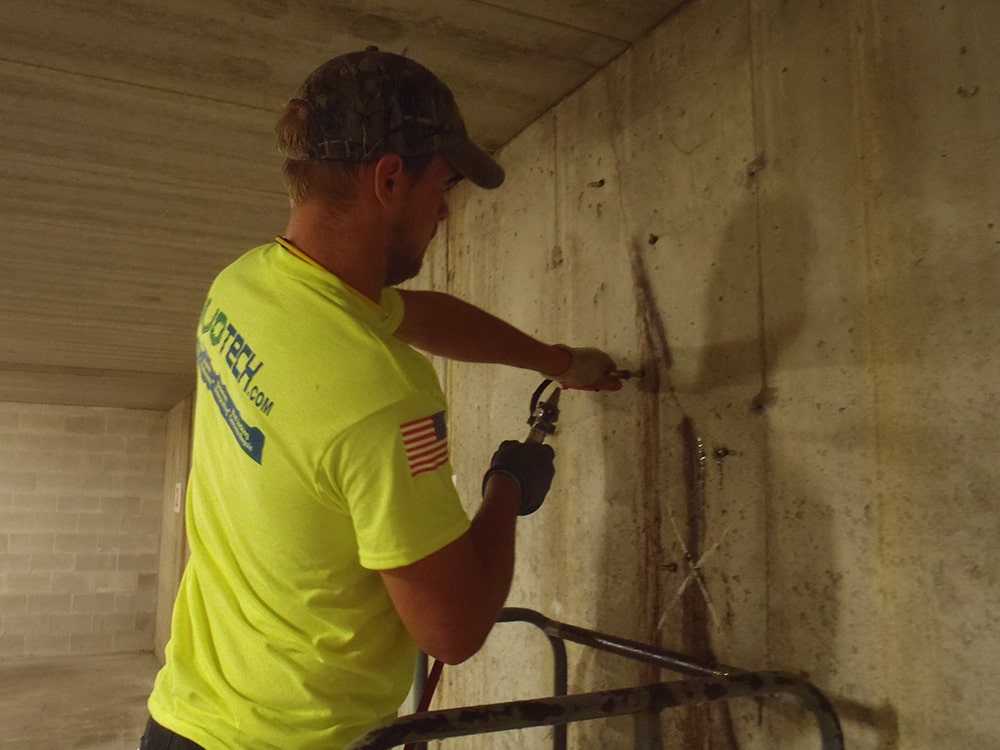 MudTech technician using crack injection to repair cracked concrete basement wall.